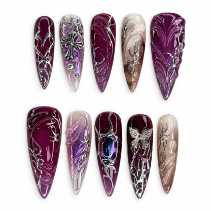 Ten Amethyst Relic press-on nails in plum, violet, smoky nude, and silver-toned raised gothic linework.