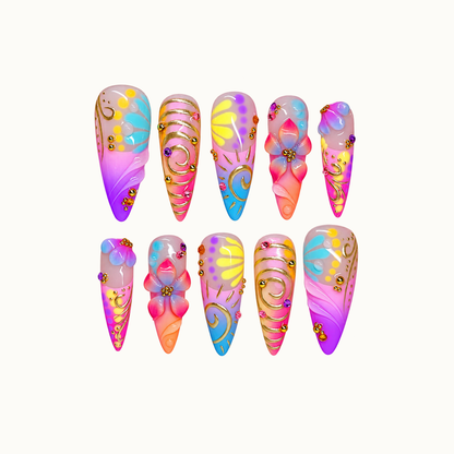Ten coordinated multicolor nails arranged in two rows on a light neutral background, featuring raised flowers, gold-colored swirls, and bright pink, purple, blue, and yellow accents.