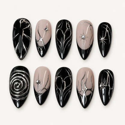 Glossy black and greige press-on nails with silver-toned abstract linework, crystal starbursts, and a raised rose-inspired accent