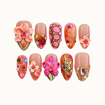 Ten decorated nails arranged in two rows on an off-white background, featuring peach and pink flowers, orange accents, gold details, and jewel-like embellishments.
