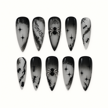 Ten black and smoky gray gothic press-on nails arranged on a light background, featuring spider webs, spiders, starbursts, and raised spider accents.