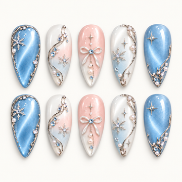 Ten coordinated nails arranged in two rows on a light neutral background, featuring blue shimmer, blush bows, snowflakes, and pearl-like accents.