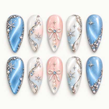 Ten coordinated nails arranged in two rows on a light neutral background, featuring blue shimmer, blush bows, snowflakes, and pearl-like accents.