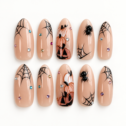 Ten glossy nude press-on nails arranged on a light background with black spiderwebs, spiders, bats, orange accents, and crystal-style details.