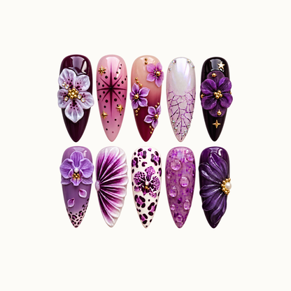 Ten purple and pink floral nails arranged in two rows on a light background, featuring raised blooms, stars, spotted patterns, and pearly accents.