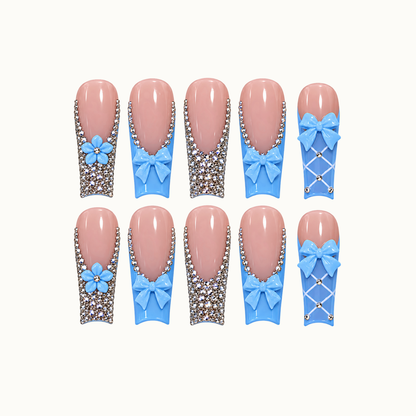 Ten blush-pink and sky-blue nails arranged in two rows on a light neutral background, with blue bows, flowers, rhinestones, and white lattice accents.