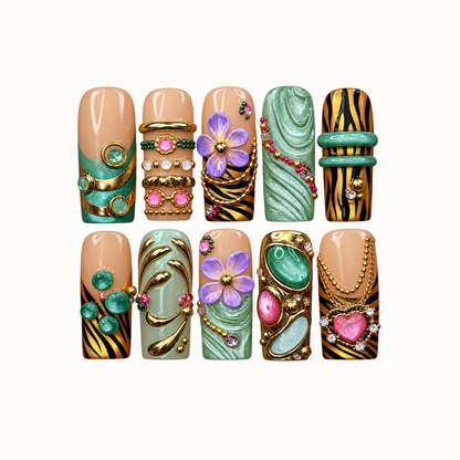Ten coordinated nails arranged in two rows on a light background, featuring green swirls, lavender flowers, black-and-gold stripes, and jewelry-inspired accents.