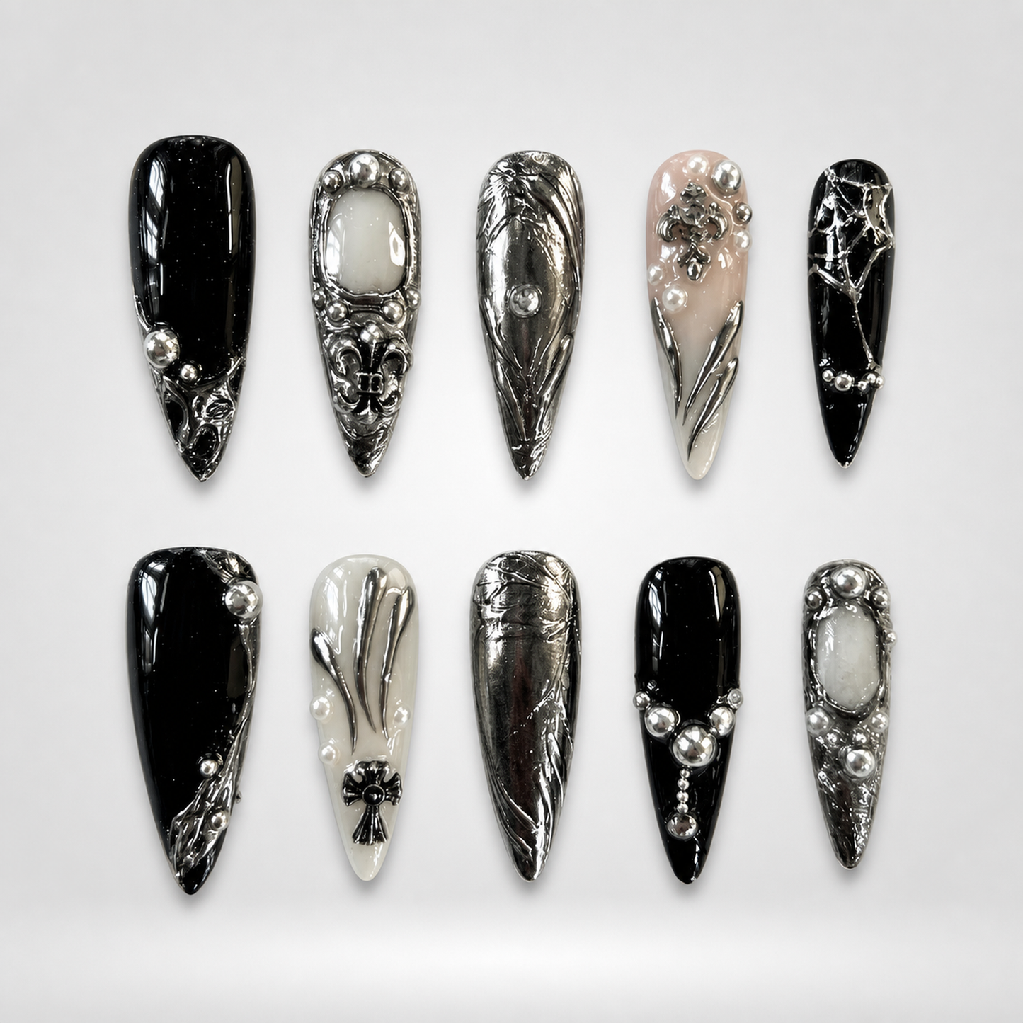 Ten coordinated gothic press-on nails in glossy black, ivory, blush nude, and reflective silver with ornate crosses, beads, and metallic details.