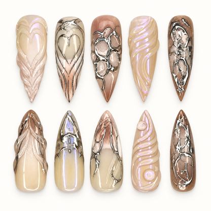 Chrome Relic press-on nail set arranged in a clear case, showing taupe, cream, and brown nails with silver-toned ornate accents.