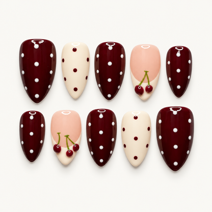 Ten glossy nails arranged in two rows on a light background, featuring burgundy and ivory polka dots with blush pink cherry accents.