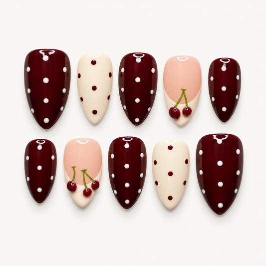 Ten glossy nails arranged in two rows on a light background, featuring burgundy and ivory polka dots with blush pink cherry accents.