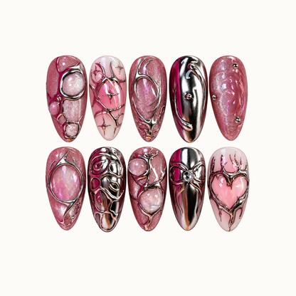 Ten pink and silver nails arranged in two rows on a light neutral background, showing chrome swirls, opalescent accents, shimmer, and a pink heart.