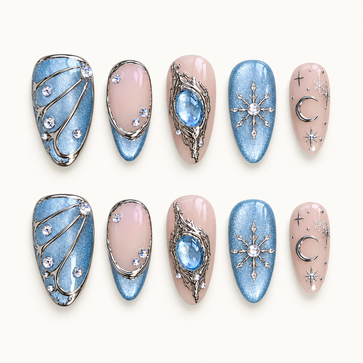Ten Moonlit Frost press-on nails arranged in two rows, showing icy blue shimmer, blush pink, silver-tone accents, snowflakes, a crescent moon, and a blue centerpiece.
