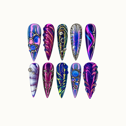 Ten pointed nails arranged in two rows on a light neutral background, with blue, magenta, violet, and teal patterns and silver-tone ornamental details.