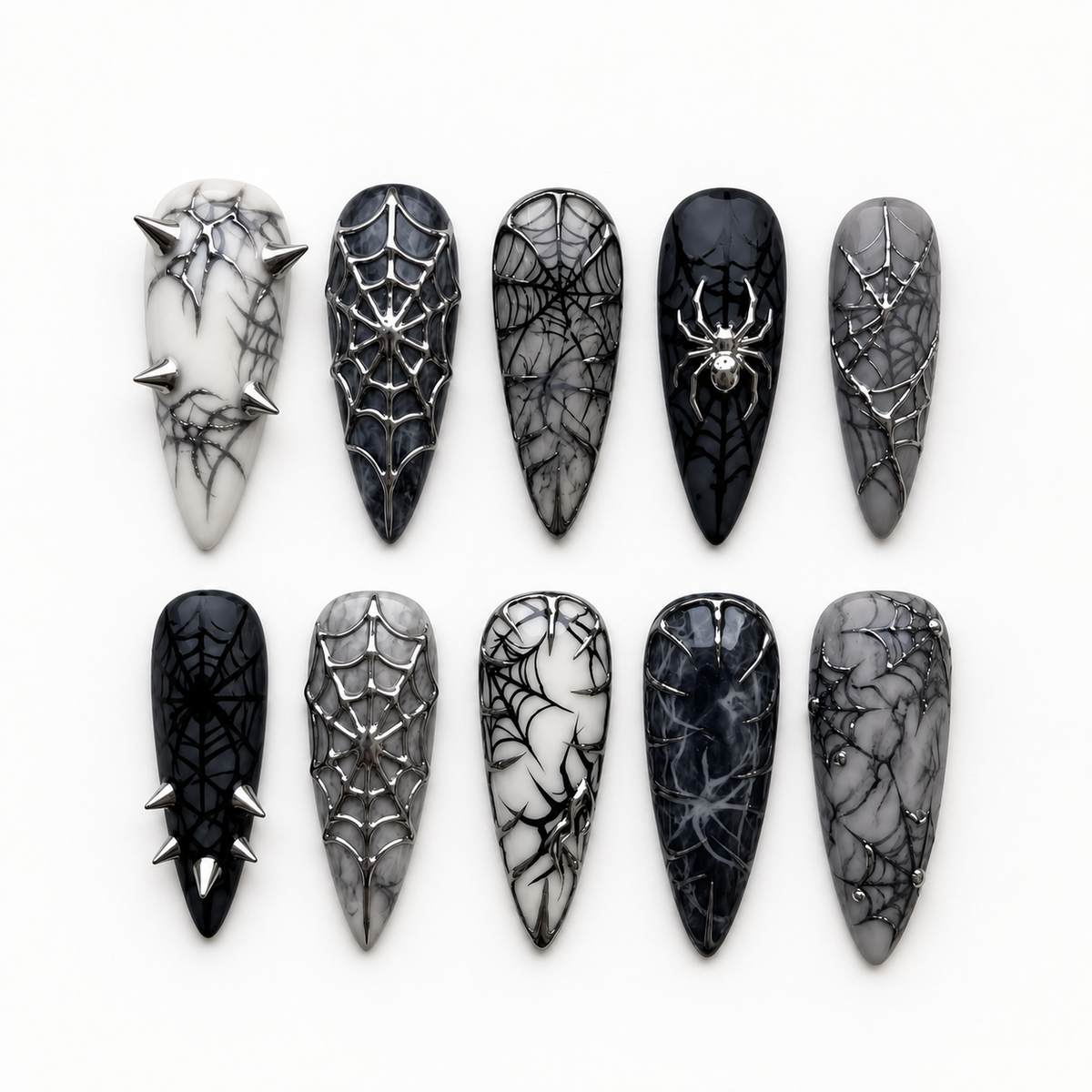 Ten long black and smoky gray press-on nails arranged on a light background, featuring spiderweb patterns, silver-toned raised accents, a spider-inspired detail, and pointed spikes.