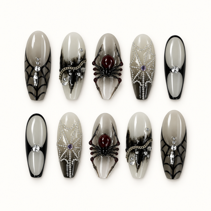 Ten glossy greige and smoky gray press-on nails arranged on a white surface, featuring black spider webs, dimensional spiders, silver beads, and crystal accents.