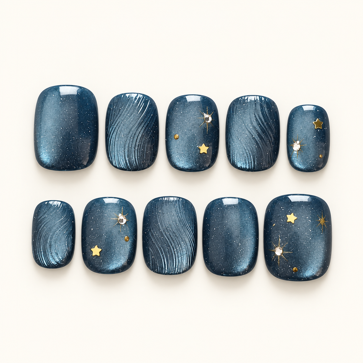 Ten navy-blue press-on nails arranged in two rows, with fine curved textures, gold stars, and bright accents against a light background.