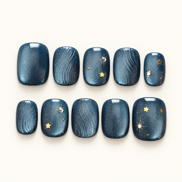 Ten navy-blue press-on nails arranged in two rows, with fine curved textures, gold stars, and bright accents against a light background.