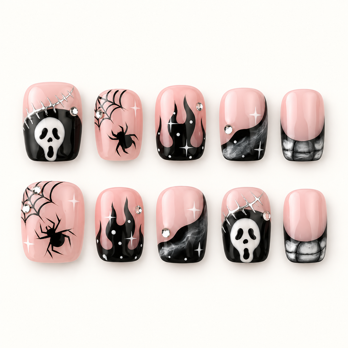 Ten coordinated blush pink and black press-on nails with spiderwebs, spiders, smoky gray details, abstract face motifs, and rhinestone-style accents on a pale neutral background.