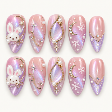 Ten pink and lilac shimmer nails arranged in two rows, featuring white bunnies, gold-toned lines, crescent moons, stars, snowflakes, and pearl-like accents.
