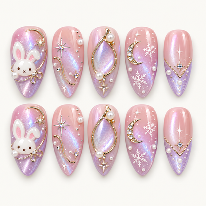 Ten pink and lilac shimmer nails arranged in two rows, featuring white bunnies, gold-toned lines, crescent moons, stars, snowflakes, and pearl-like accents.