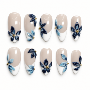 Ten glossy nude beige nails arranged in two rows, with white French tips, navy and pale blue floral accents, and gold-tone beads.