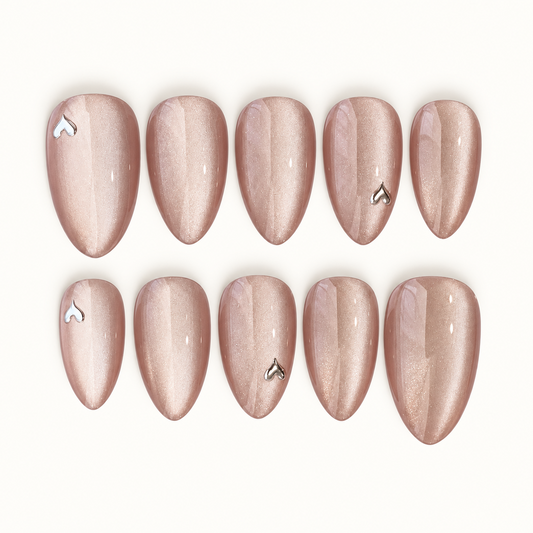 Ten blush-nude shimmer nails arranged in two rows on a light neutral background, with glossy reflections and four silver-toned heart accents.