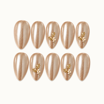 Ten champagne shimmer nails arranged in two rows on a light neutral background, with gold-tone holly leaves and ivory pearl-like clusters on four accent nails.