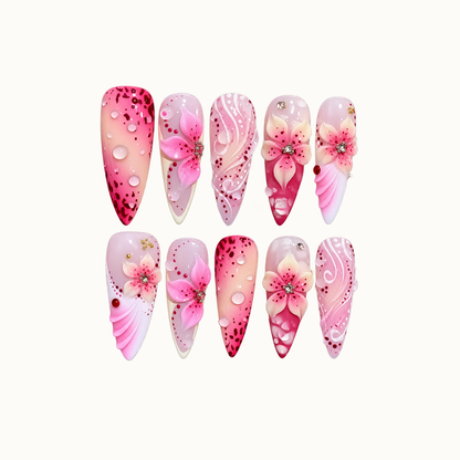 Ten pink nails arranged in two rows on an off-white background, featuring raised flowers, clear droplets, white swirls, and berry-colored speckles.