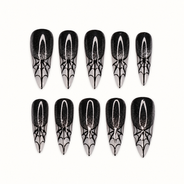 Ten glossy black press-on nails with subtle sparkle, silver-gray pointed tips, and black spiderweb designs on a light neutral background.