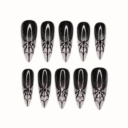 Ten glossy black press-on nails with subtle sparkle, silver-gray pointed tips, and black spiderweb designs on a light neutral background.