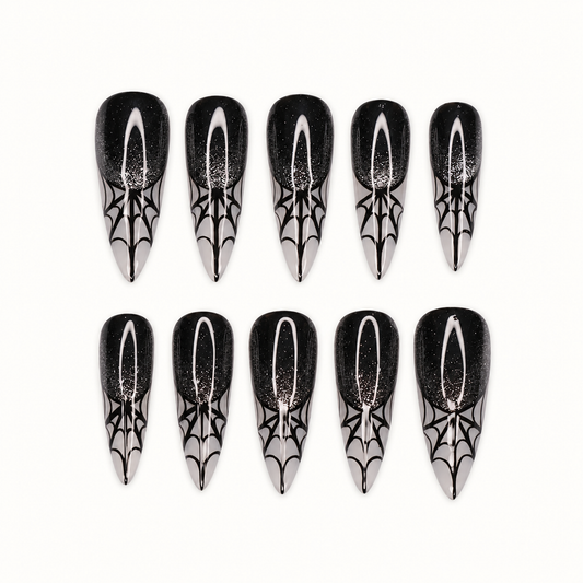 Ten glossy black press-on nails with subtle sparkle, silver-gray pointed tips, and black spiderweb designs on a light neutral background.
