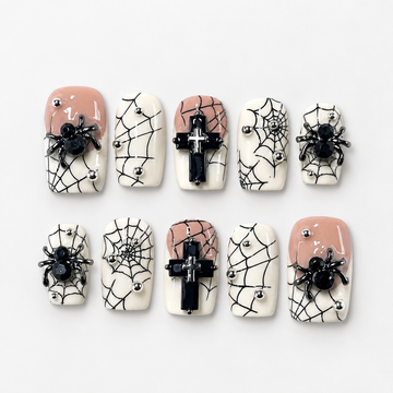Ten coordinated Eternal Web press-on nails arranged in a clear case, with black spiderwebs, raised spiders, black crosses, ivory and blush accents, and metallic studs.