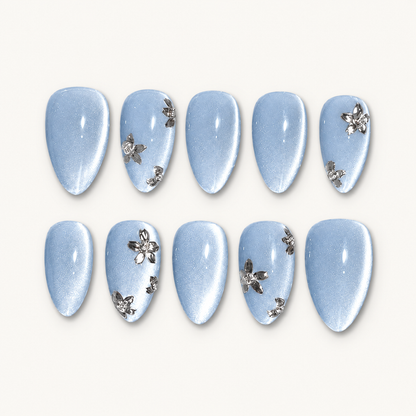 Ten pale blue shimmer nails arranged in two rows on an off-white background, with silver-toned flowers on select nails.
