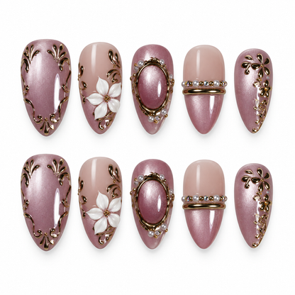 Ten mauve and blush nude nails arranged in two rows on a light background, featuring gold-toned scrollwork, white flowers, and oval framed accents.