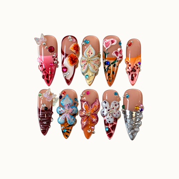 Ten nude-base nails in two rows with raised multicolor flowers, butterfly accents, colorful gems, and pink, orange, burgundy, and silver details.