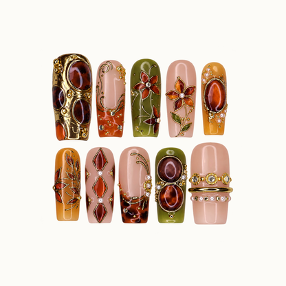 Ten decorated nails in two rows on a light neutral background, featuring olive, blush, mustard, amber-toned accents, flowers, and gold-tone filigree.