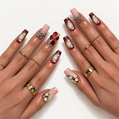 Hand model mockup showing the pink and burgundy nail design with dimensional red floral accents, ornate silver-tone details, and pale droplet embellishments.