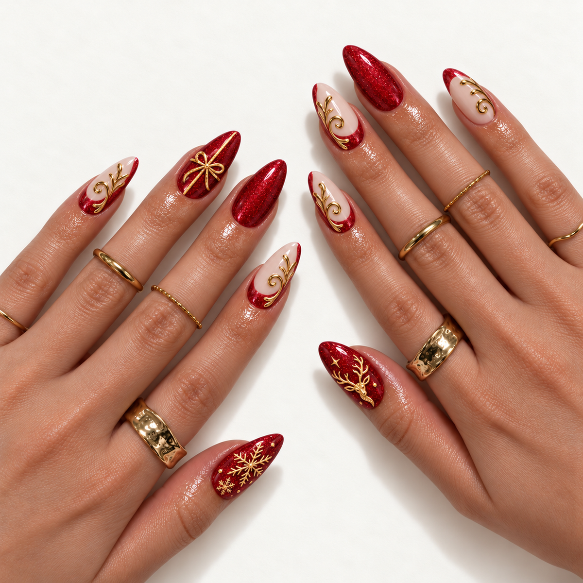 Two hands modeling pointed red and blush nails with gold-tone holiday accents, including a bow, snowflakes, reindeer, and leafy scrolls.