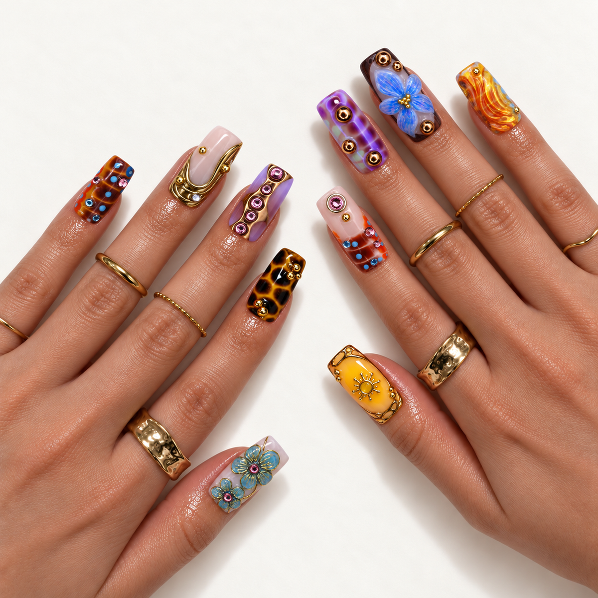 Two hands model the mixed nail design with raised blue flowers, amber spots, a yellow sun motif, lavender patterns, and gold-tone accents.
