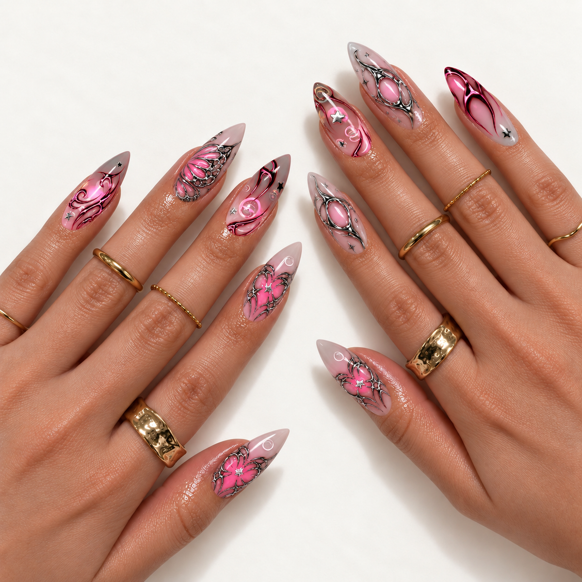Two hands wearing pointed pink and gray nails with silver wing-like outlines, magenta swirls, and star accents, styled with gold rings.
