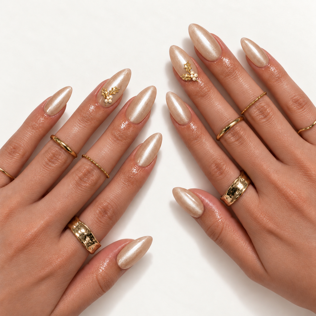 Hand model mockup showing champagne shimmer nails with gold-tone holly and pearl-like accents, styled with gold-tone rings.