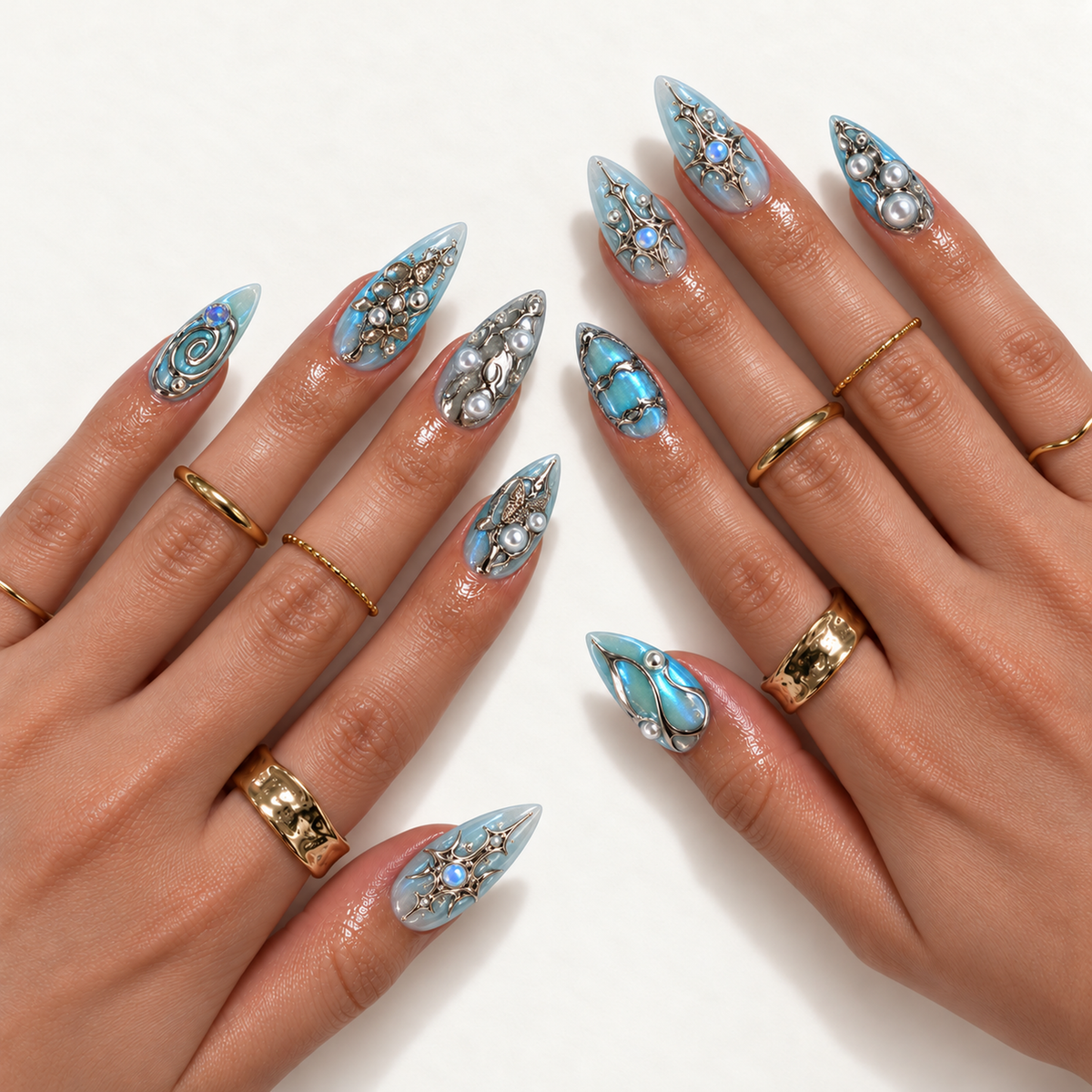 Hand model mockup showing pointed blue nails with reflective silver-tone ornament, butterfly motifs, starbursts, and pearl-like accents, styled with gold-tone rings.
