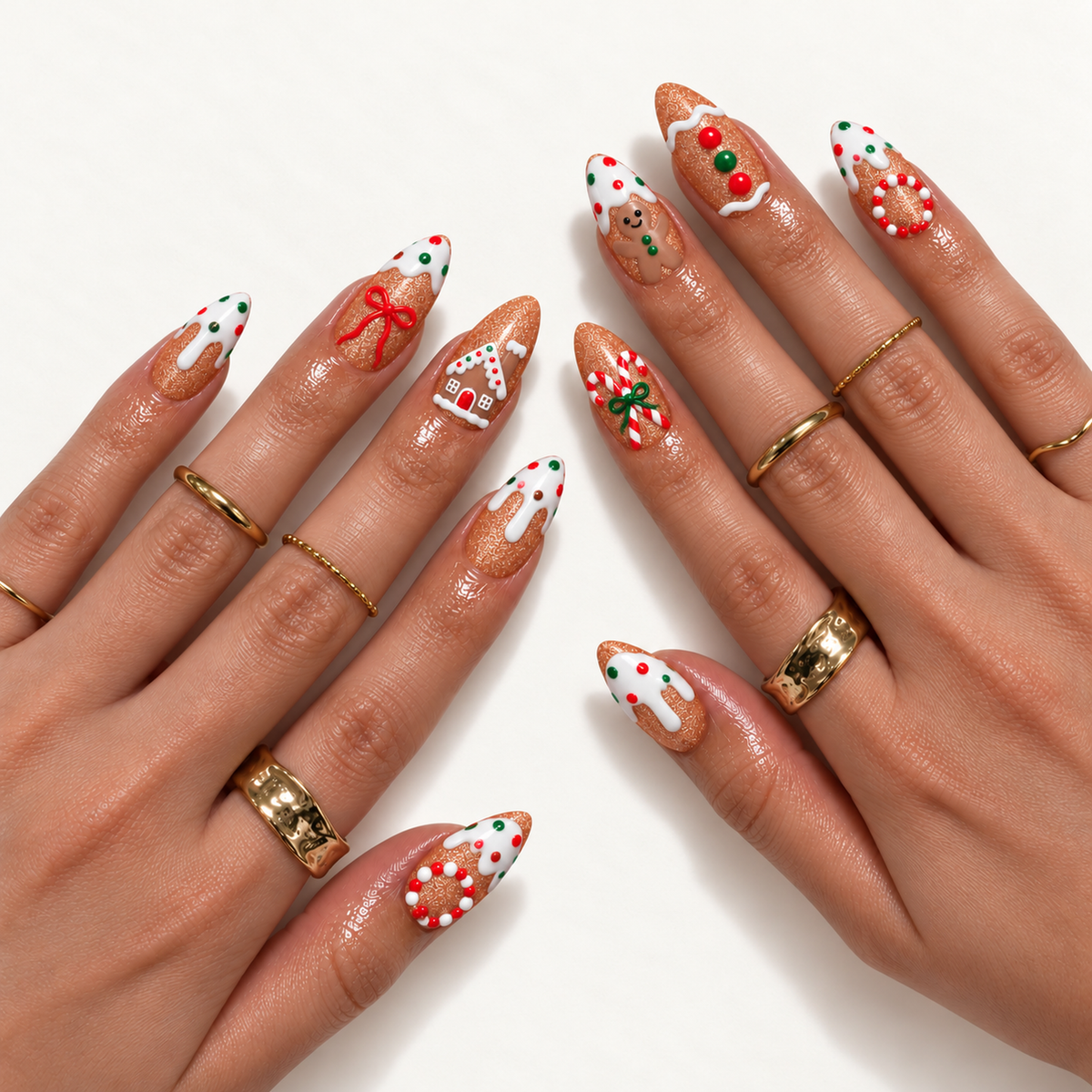 Two hands wearing pointed gingerbread-themed nails with white icing, red-and-green accents, candy canes, bows, and a miniature house, styled with gold-toned rings.