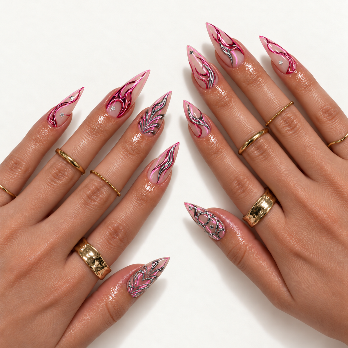 Two hands wearing pointed pink and silver abstract nails with tiny star accents, styled with gold-tone rings against a light background.