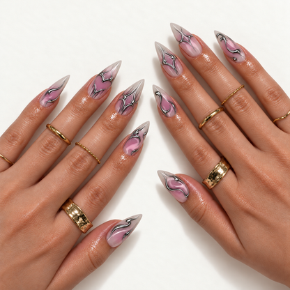 Hand model mockup showing pink and mauve gradient nails with pointed tips, silver chrome-look heart outlines, and flowing accents, styled with gold-tone rings.
