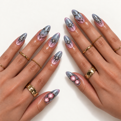 Hand model mockup showing silver-gray and pink gradient nails with heart outlines, starbursts, web-like accents, and pink details, styled with gold-tone rings.