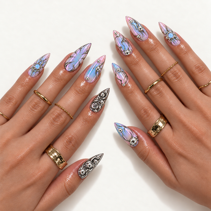Hand model mockup showing pointed pastel iridescent nails with silver ornamental lines and metallic swirl accents, styled with gold-tone rings.