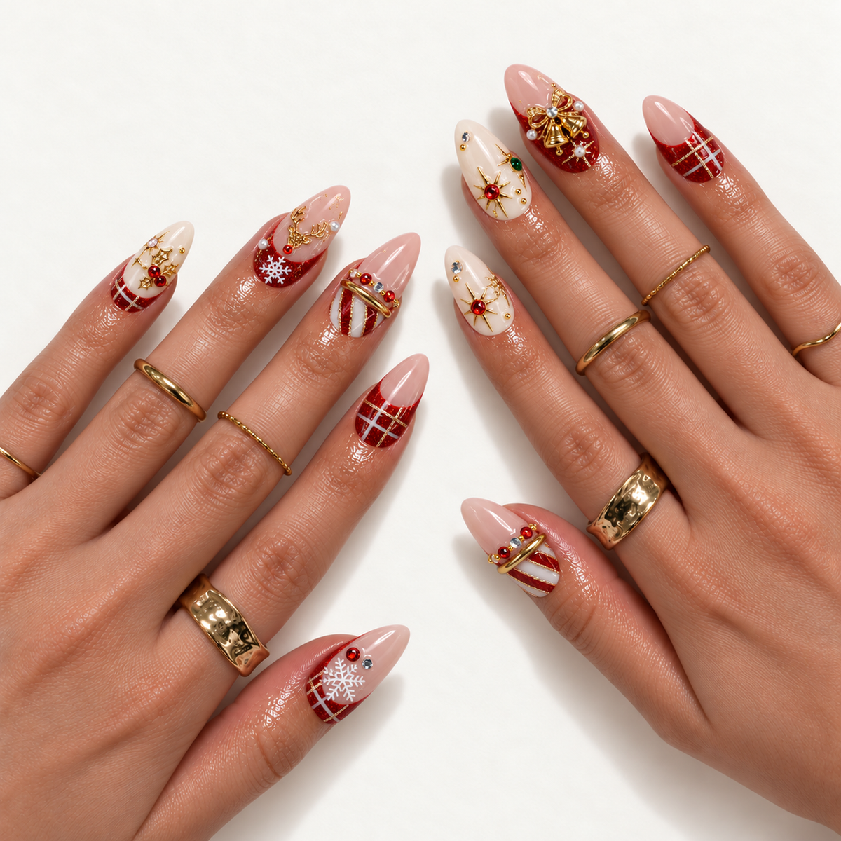 Hand model mockup showing pointed Christmas nails with red glitter tips, ivory accents, gold-tone bells and reindeer, white snowflakes, and jewel details.