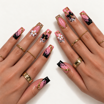 Hand-model mockup showing pink leopard nail art with black tips, white and black floral accents, and sparkling gold-tone details, styled with gold-tone rings.